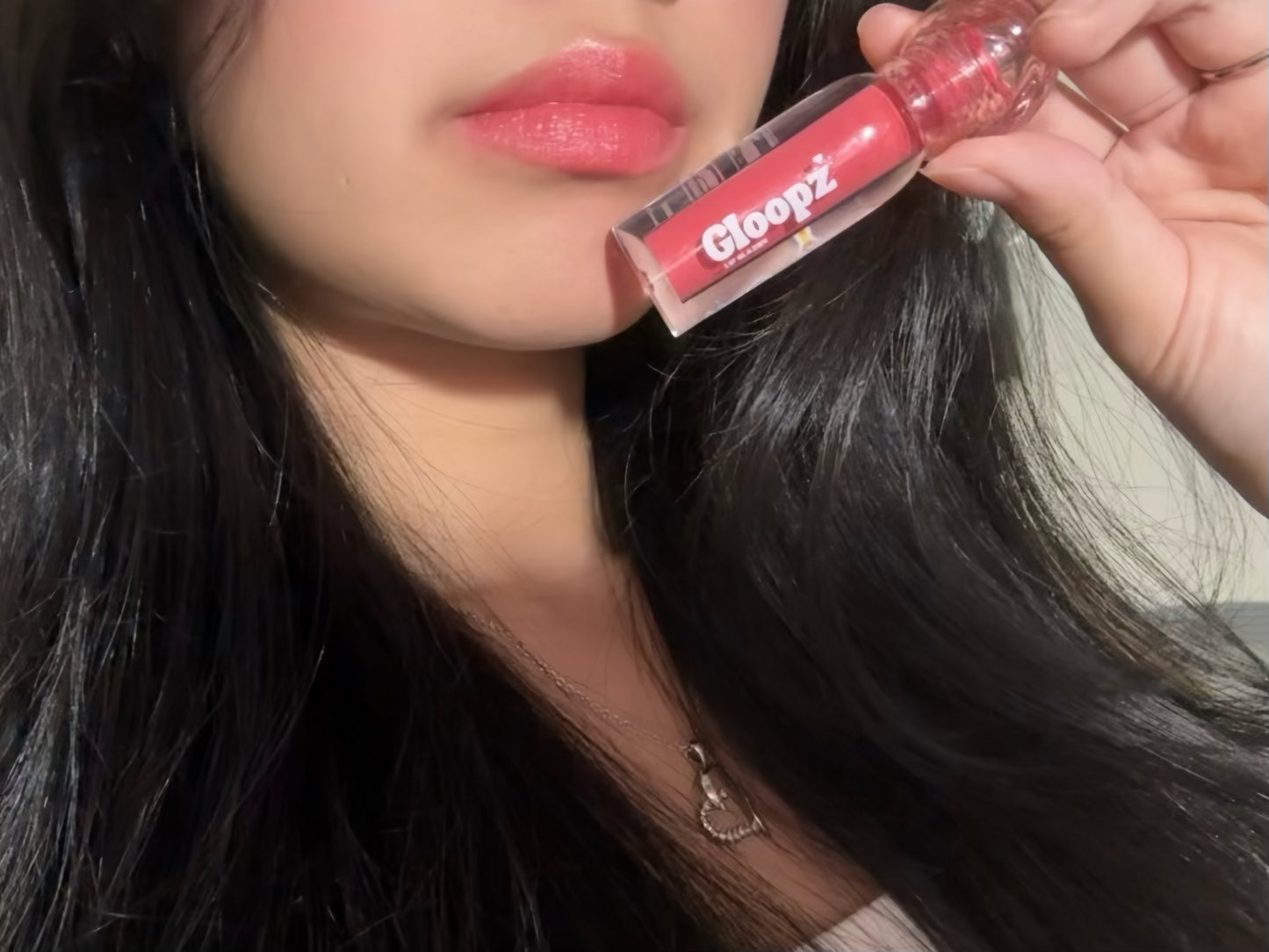 Person holding a pink lip gloss labeled 'Gloopz' near their lips.