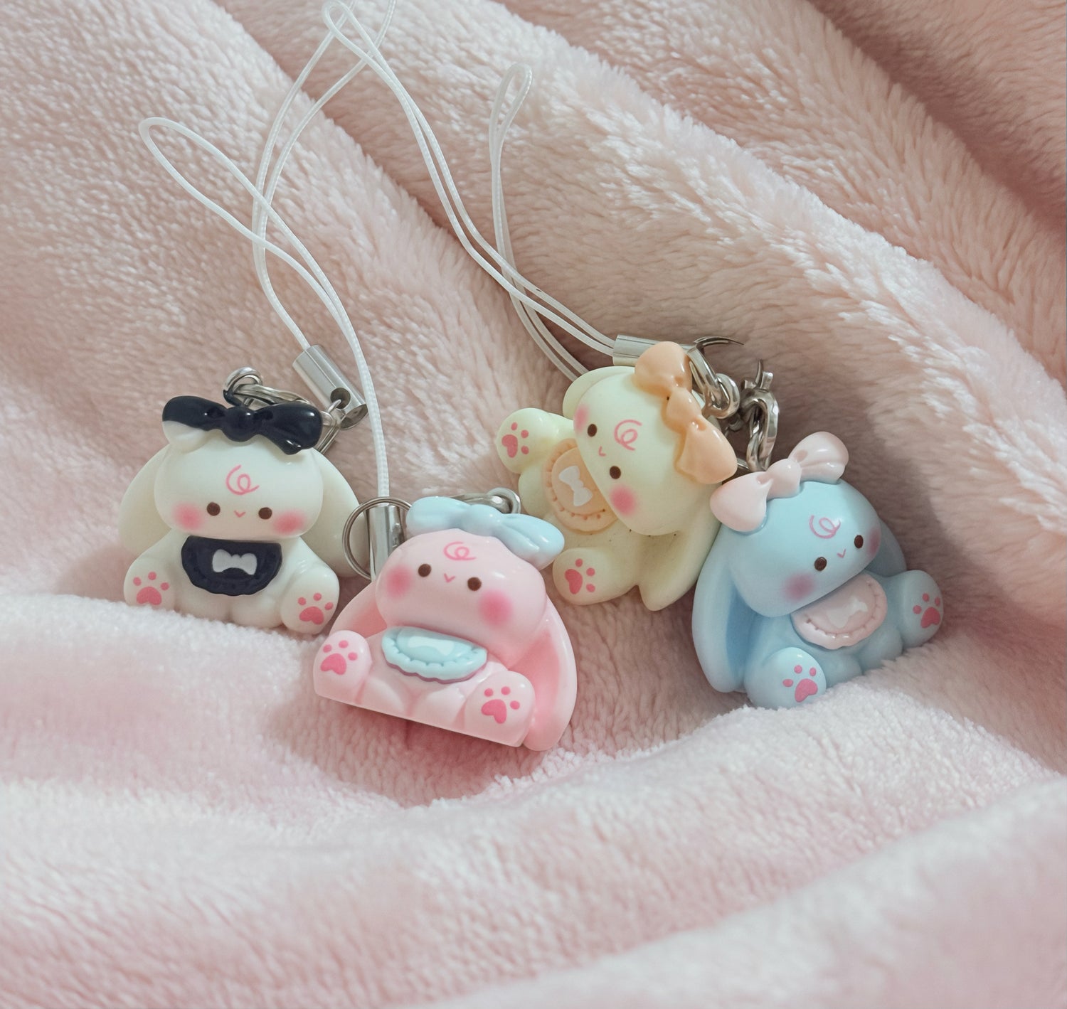 Four cute animal-themed phone charms on a soft pink fabric background