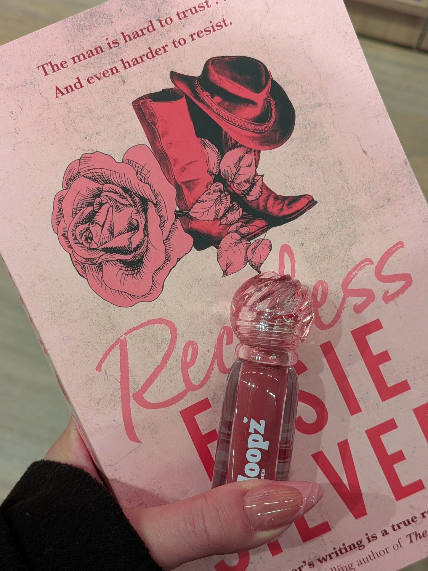 Book with pink cover featuring a rose and cowboy hat, held by a hand with a clear lip gloss.