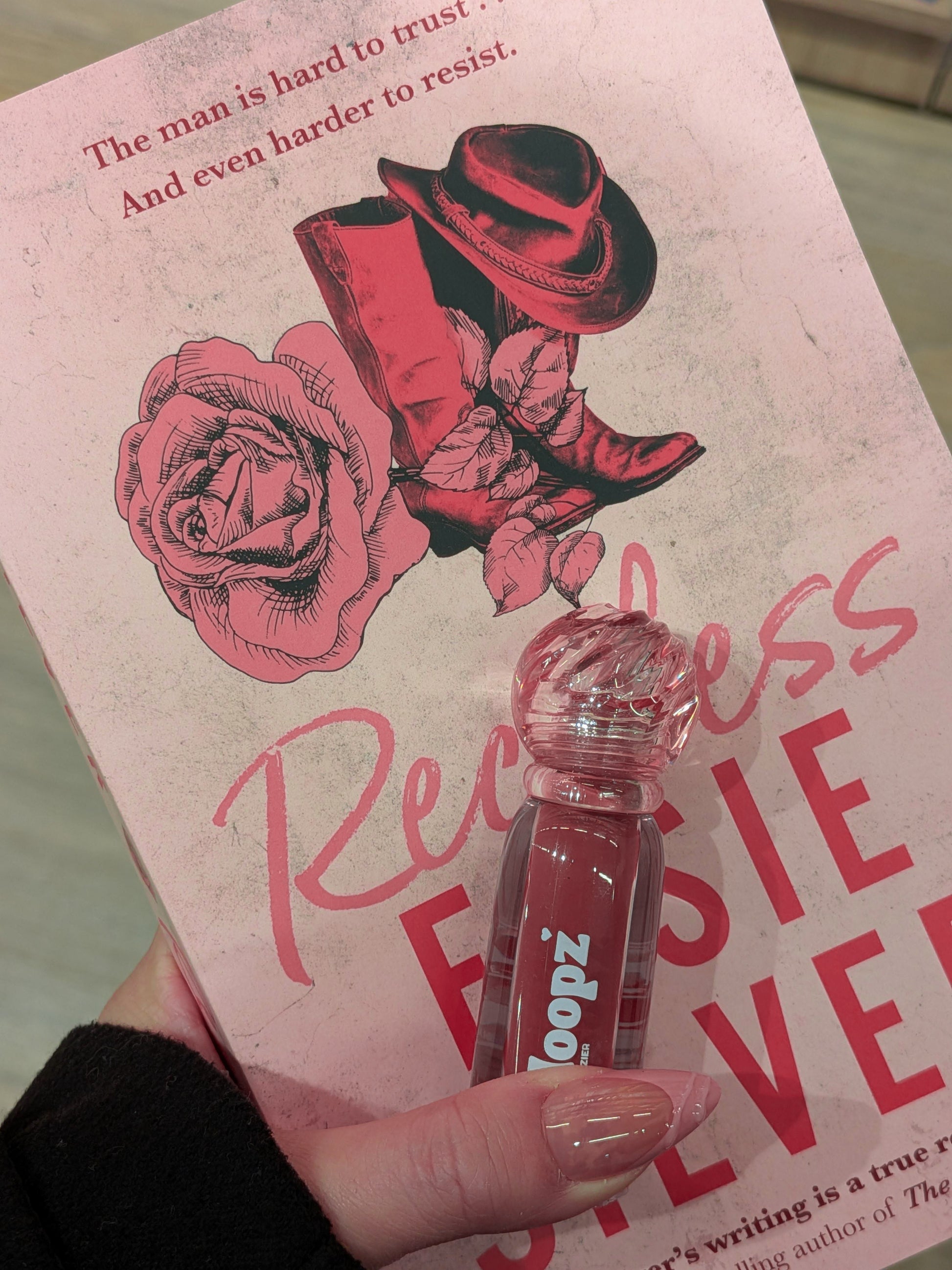 Book with pink cover featuring a rose and cowboy hat, held by a hand with a clear lip gloss.