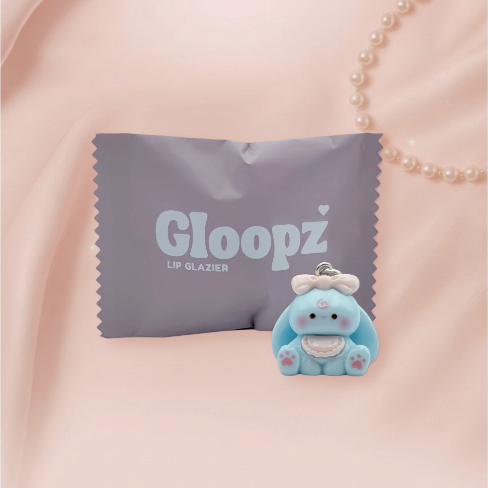 Blue bunny with a bow next to a Gloopz lip glazier pouch on a pink background