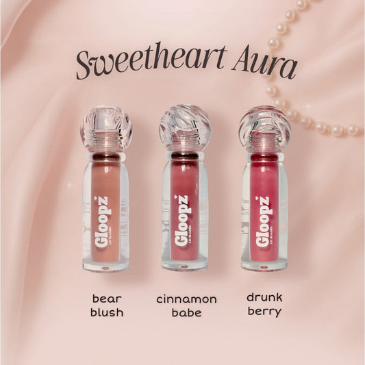 Three lip glosses from Gloopz with names 'bear blush', 'cinnamon babe', and 'drunk berry' on a pink background.
