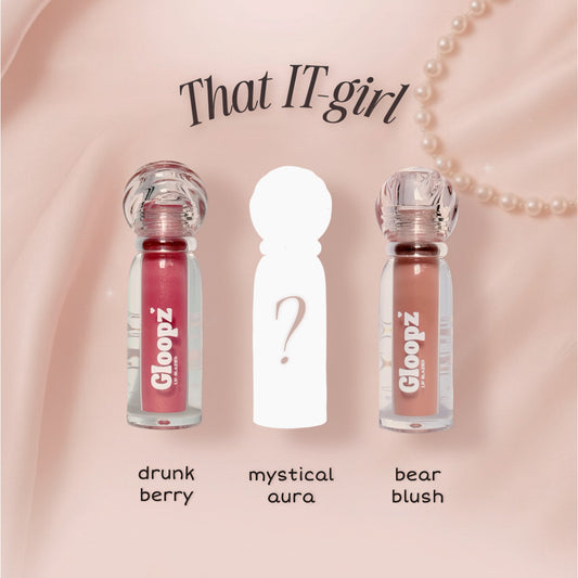 Three lip gloss bottles with labels 'drunk berry', 'mystical aura', and 'bear blush' on a pink background.