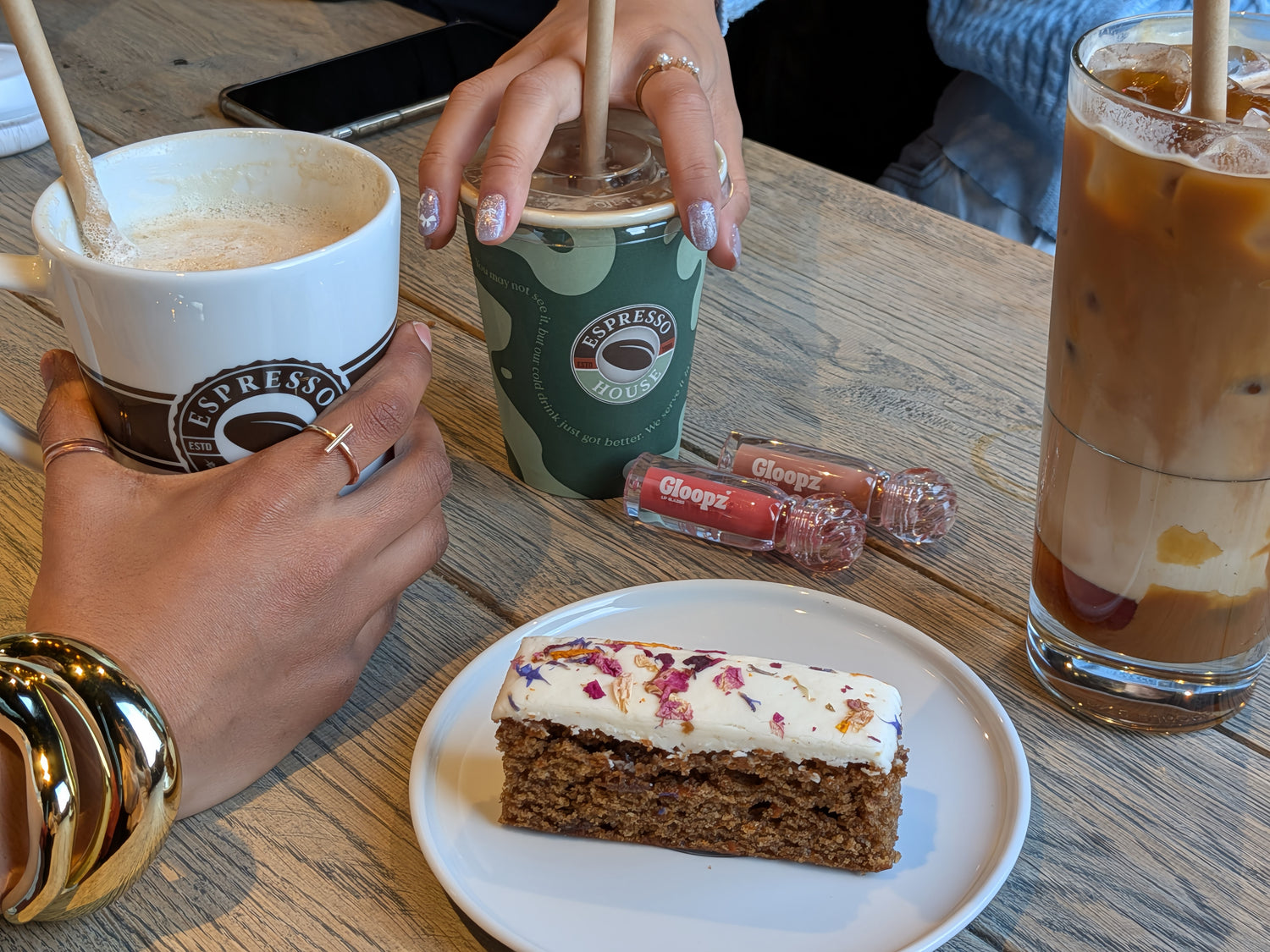 Person holding a cup of coffee with a slice of cake and a drink on a wooden table.